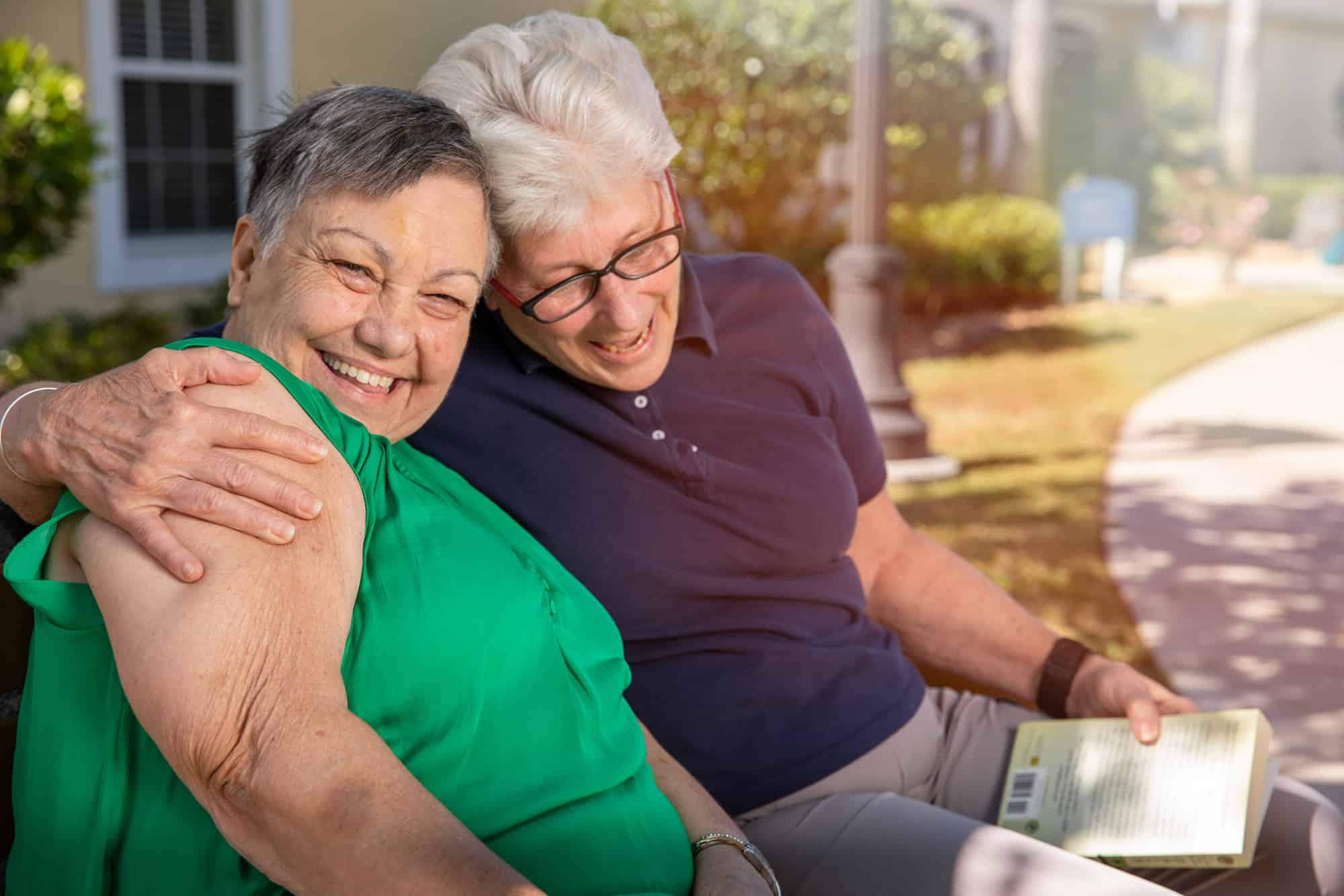 two elderly care home residents sitting outside on a bench, man has his arm around the woman