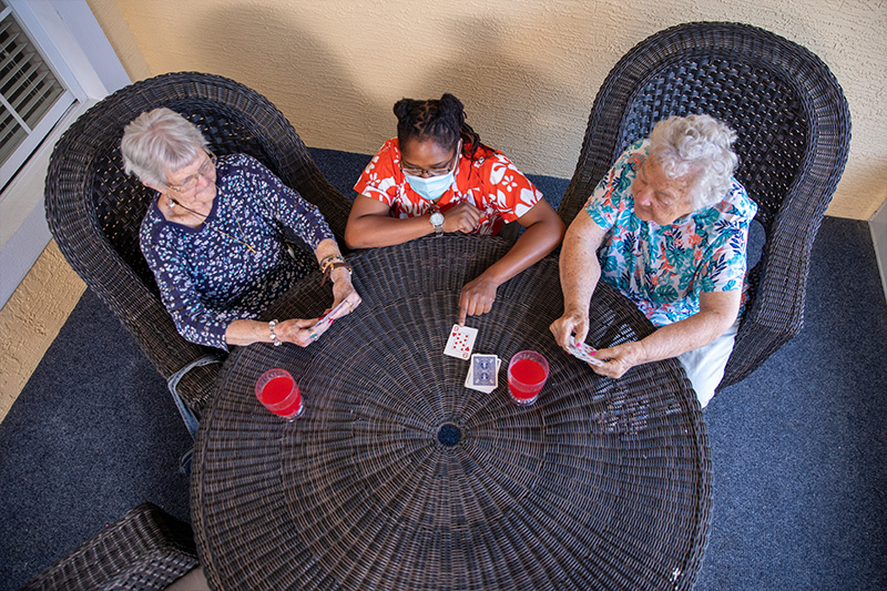 two senior care facility residents and care provider participating in a card game