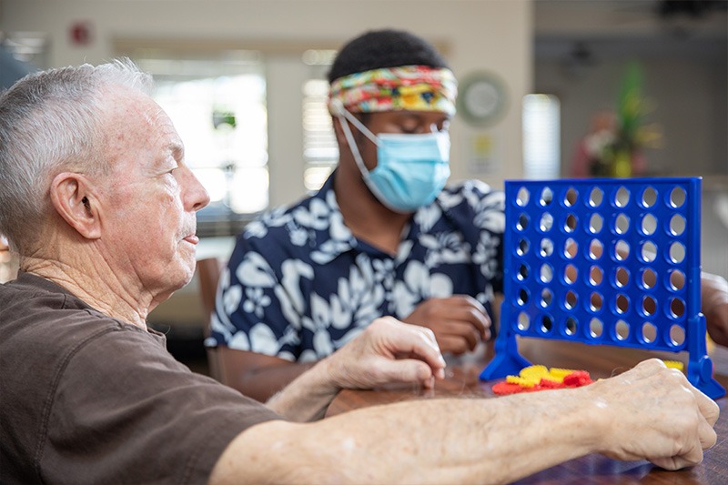 elderly male resident playing connect 4 with care giver